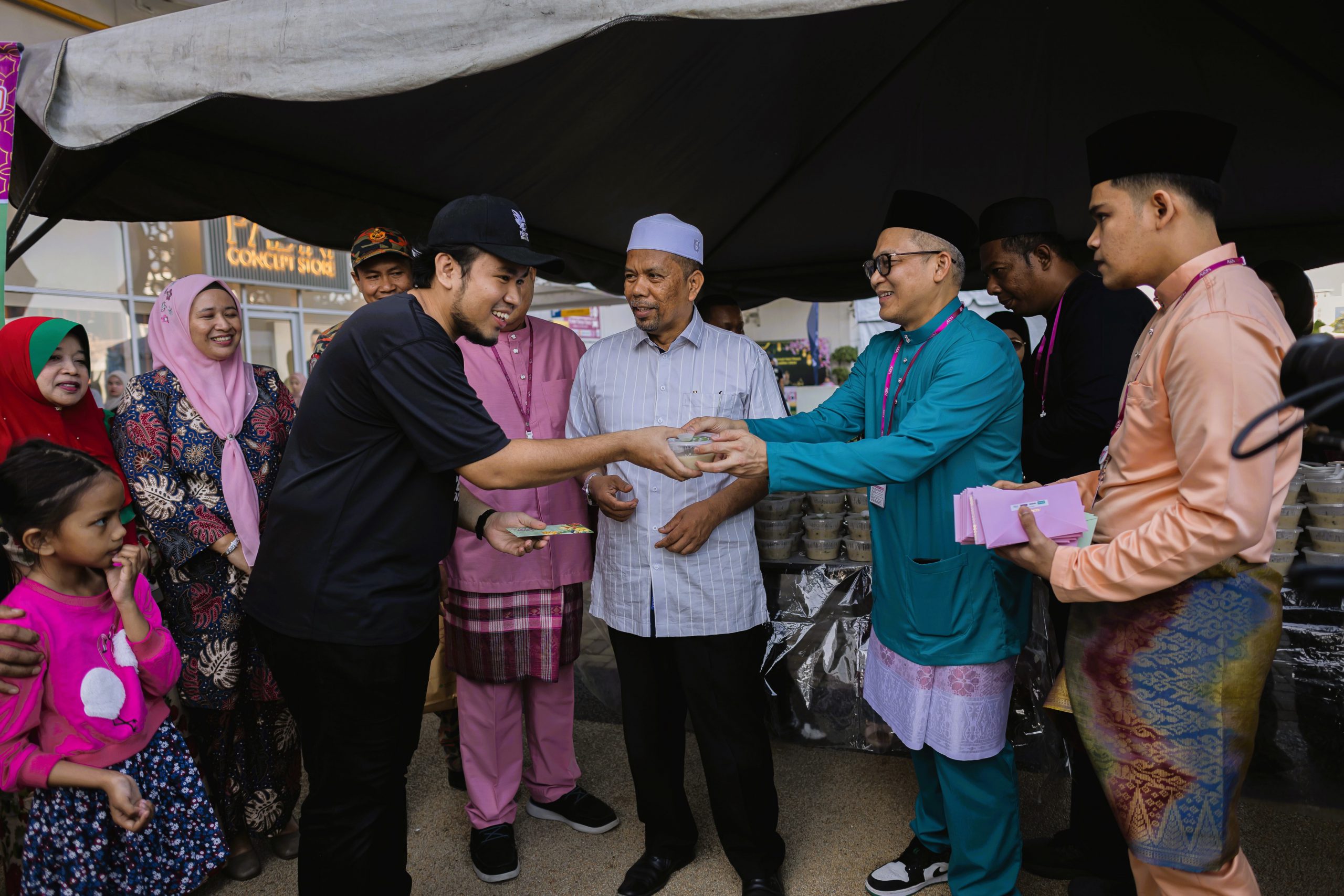 Dr Kasuma Satria (berbaju hijau) turut sama membantu mengagihkan bubur lambuk kepada pengunjung AEON Mall Kota Bharu.